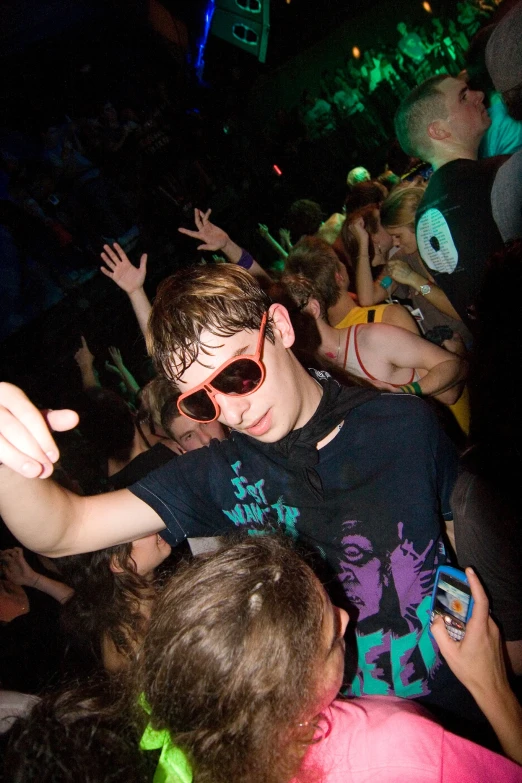 a crowd of people at a concert with a male wearing sunglasses and a black shirt with hands in the air