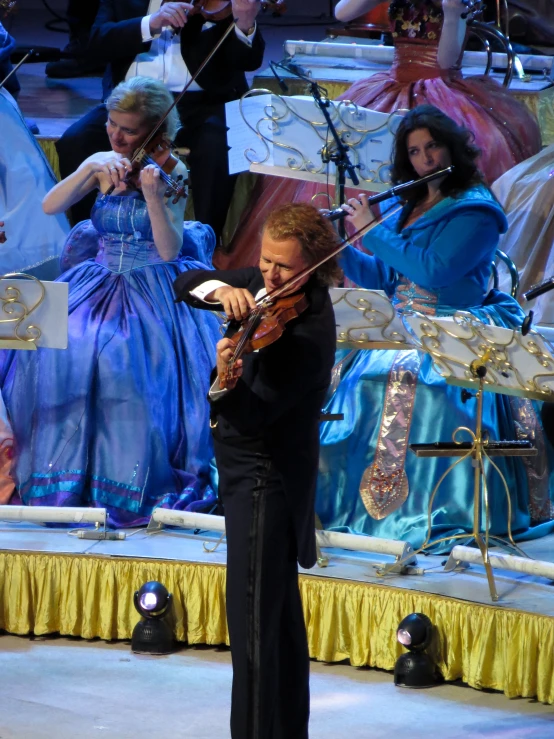 a violinist standing next to a conductor in front of other people