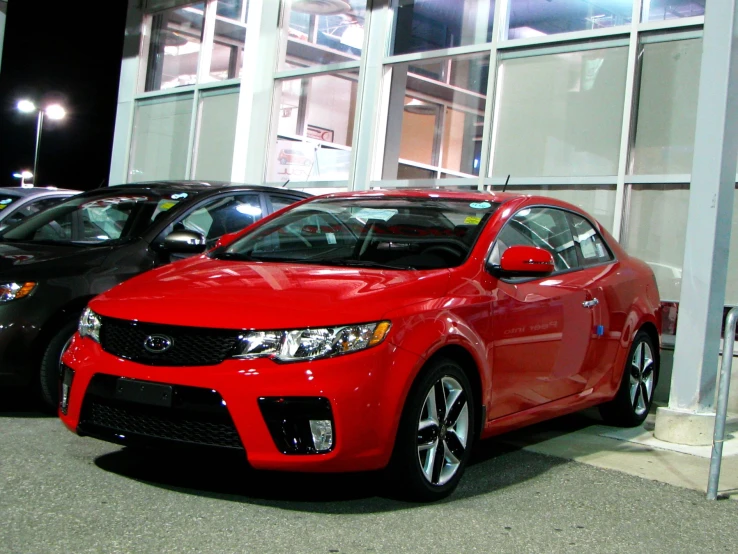 the red sports car is parked on the lot in front of the building