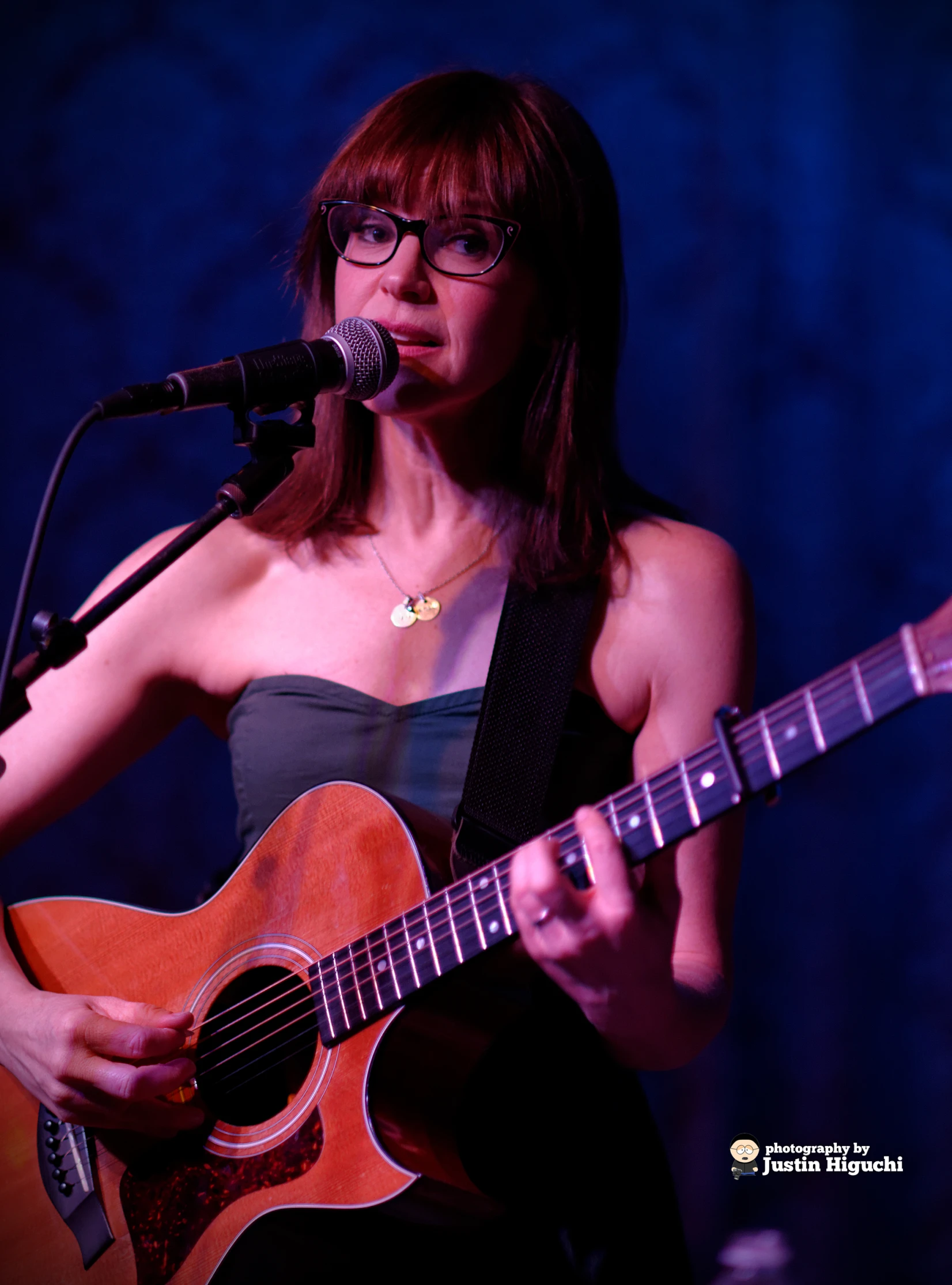 a woman standing behind a microphone while playing a guitar