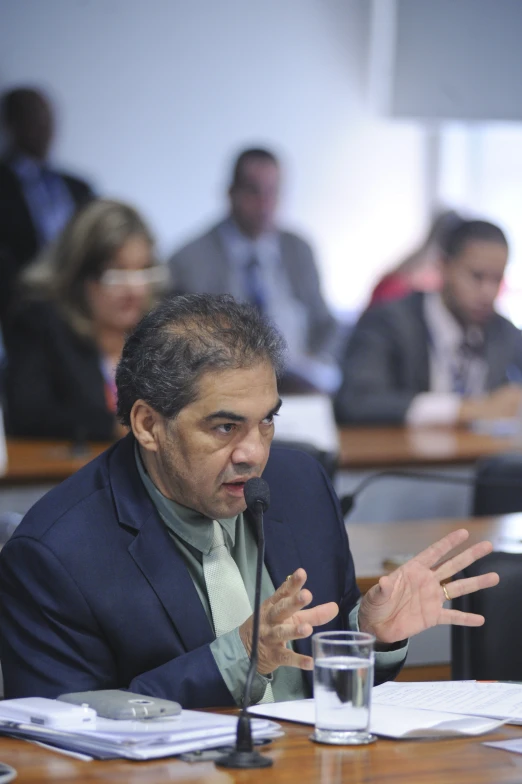 an older man in a suit sits at a conference table