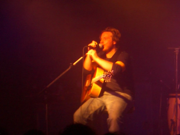 a man playing a guitar while standing in front of microphones