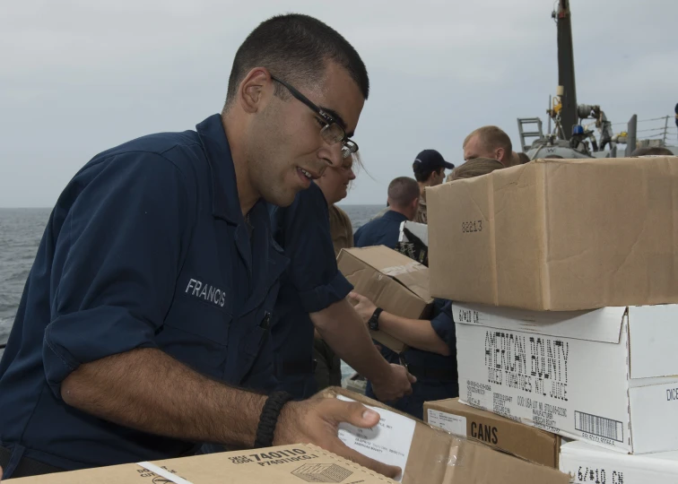 a man in navy uniform holds two boxes of pizza on his hand