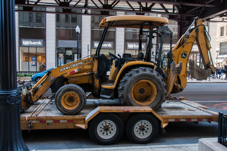 an excavator loader on a flatbed trailer in front of buildings