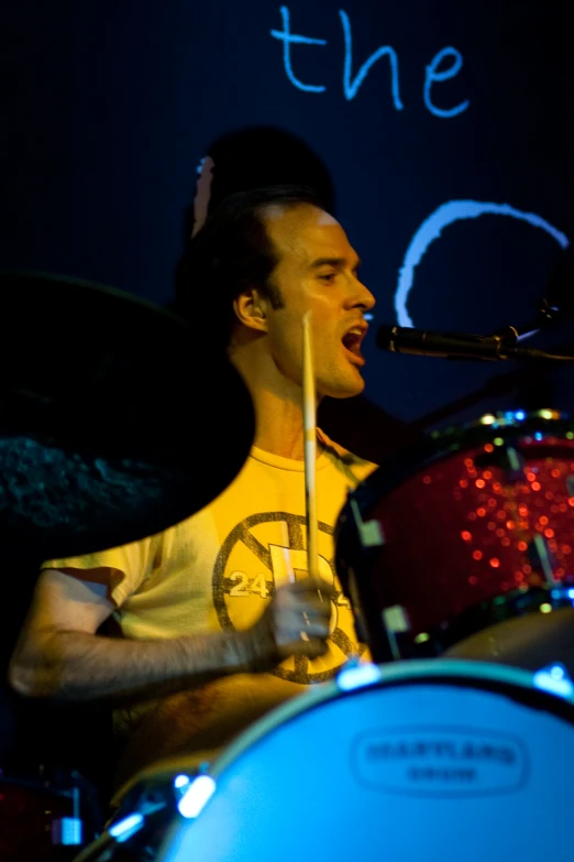 a guy playing the drums and singing into a mic