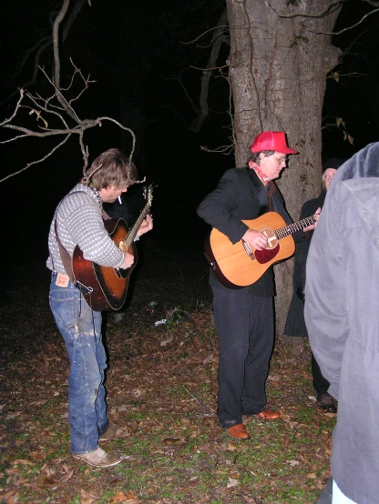 a person playing a guitar and another standing with a hat on