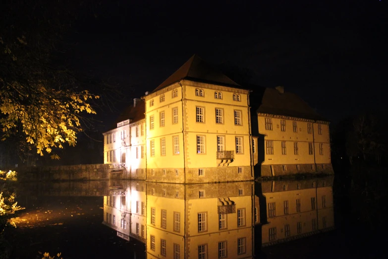 a large building sitting above a lake next to trees