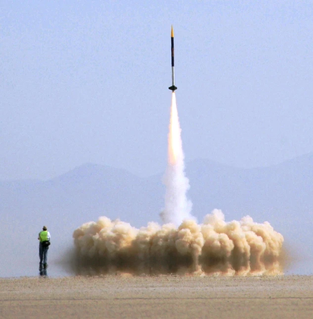 a man stands near the burning rocket in a desert area