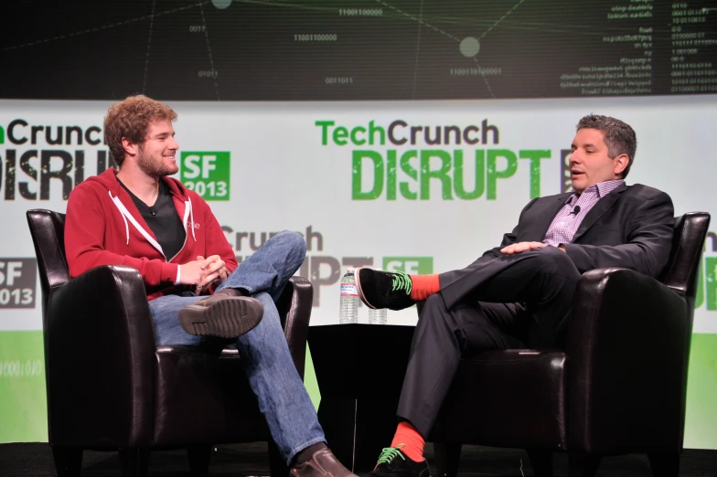 two men sitting in black chairs and one is talking on the phone