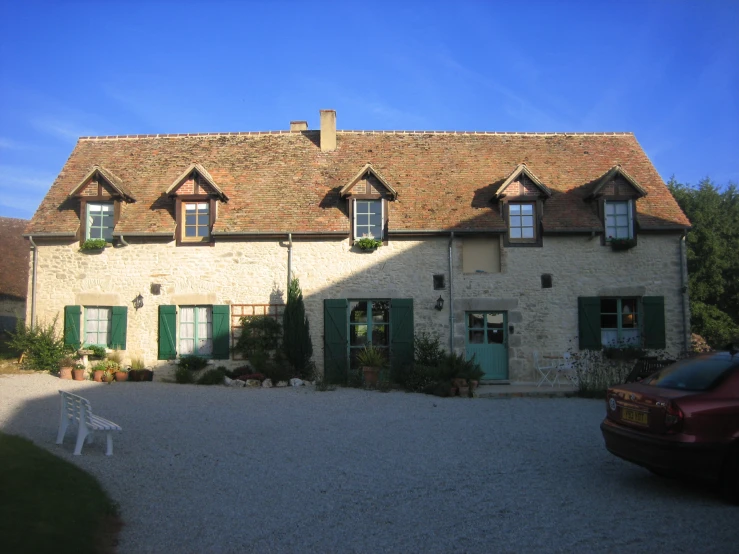 a brick house with green doors on a gravel driveway