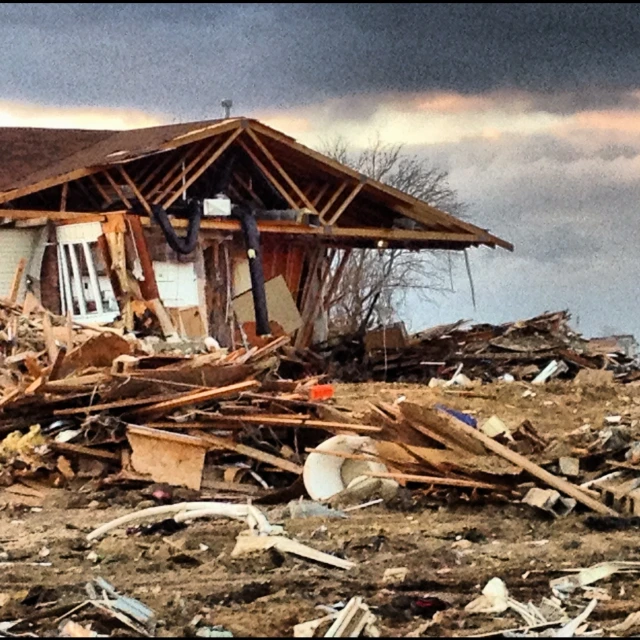 a house stands in the rubble while other houses sit nearby