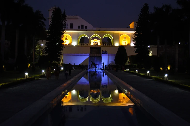 an outdoor garden with lights surrounding and reflecting pool at night