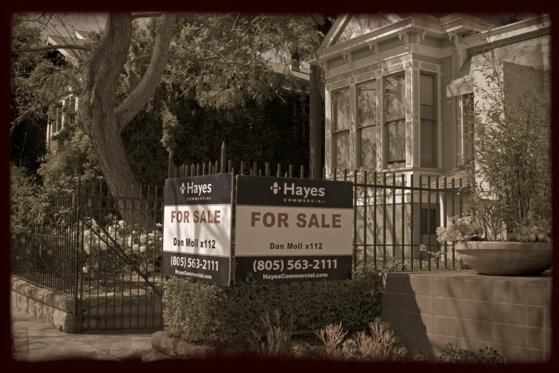 a sign and a large house behind it for sale