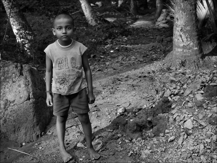 a little boy standing next to a tree