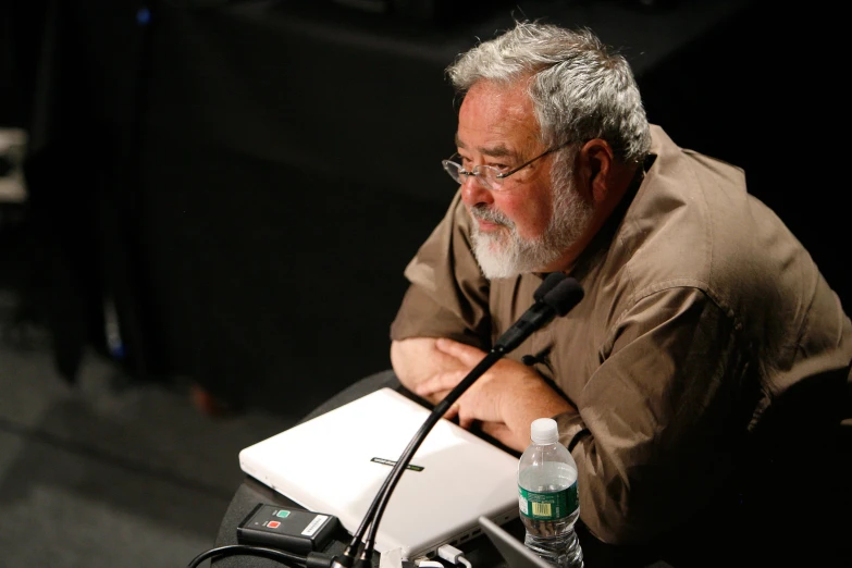 a man in brown shirt with microphone on stage