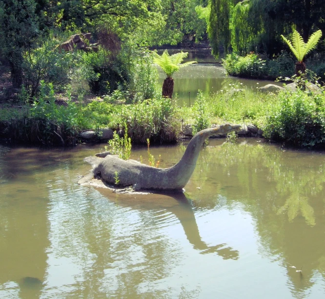 a dinosaur in water near bushes and trees