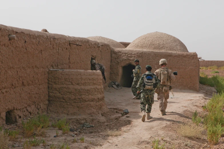 four people walking in a village with mud structures