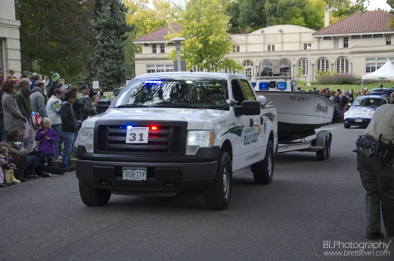 two police trucks in a parade with a boat on its bed