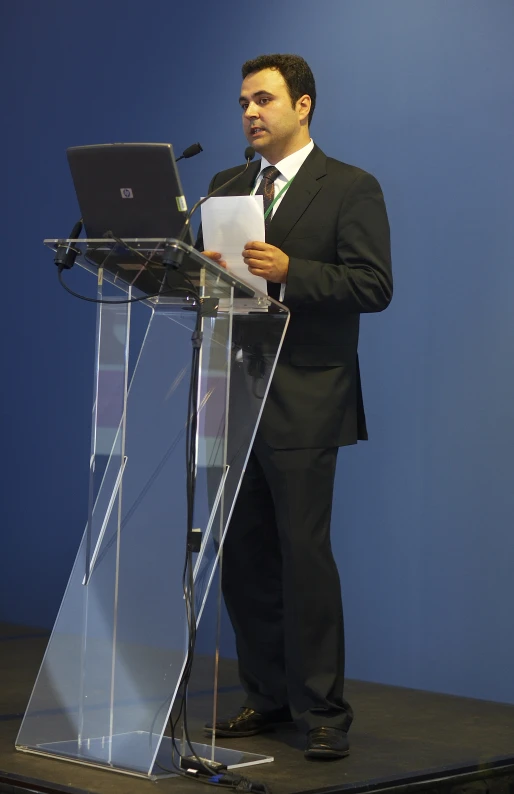 a man in a suit standing at a podium with a laptop