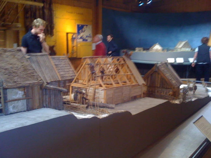 people looking at a model wooden building made out of rafts