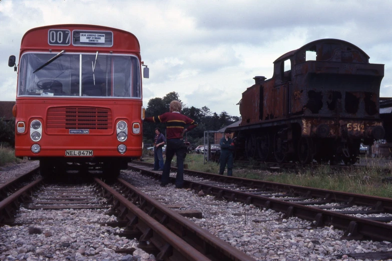 a red bus on train tracks and people near it