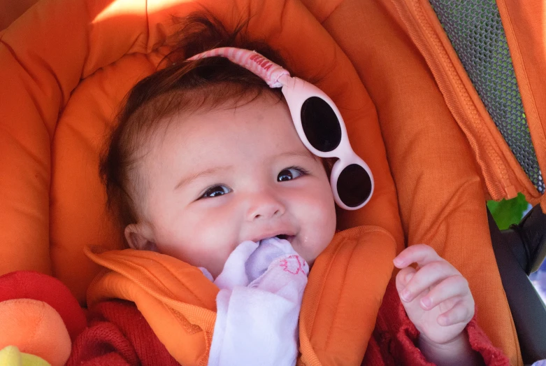 a small baby lying in a baby car seat with large toothbrushes