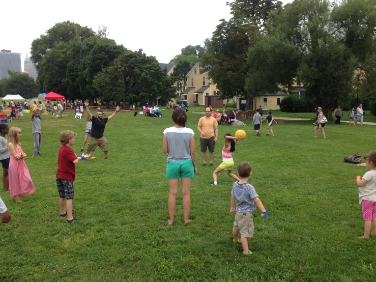 a group of children and adults are standing in the grass and playing outside