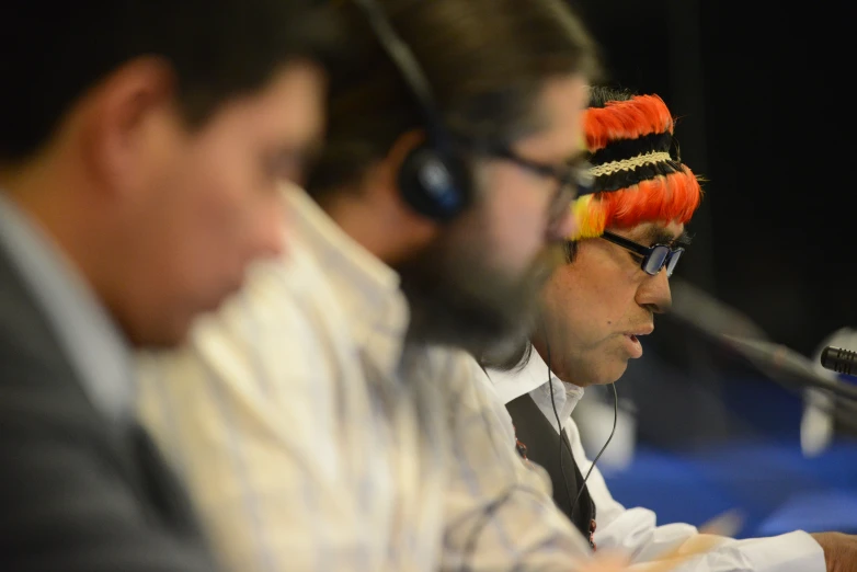 a number of men sitting at a table wearing headphones