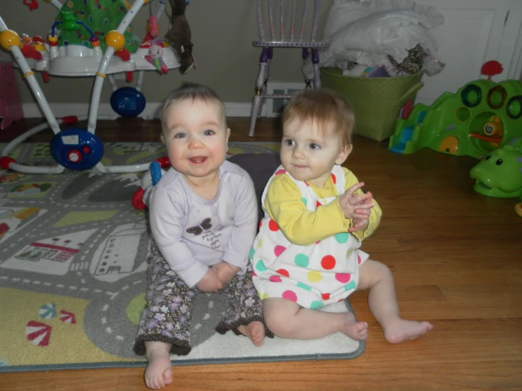 two babies sitting on a toy play mat