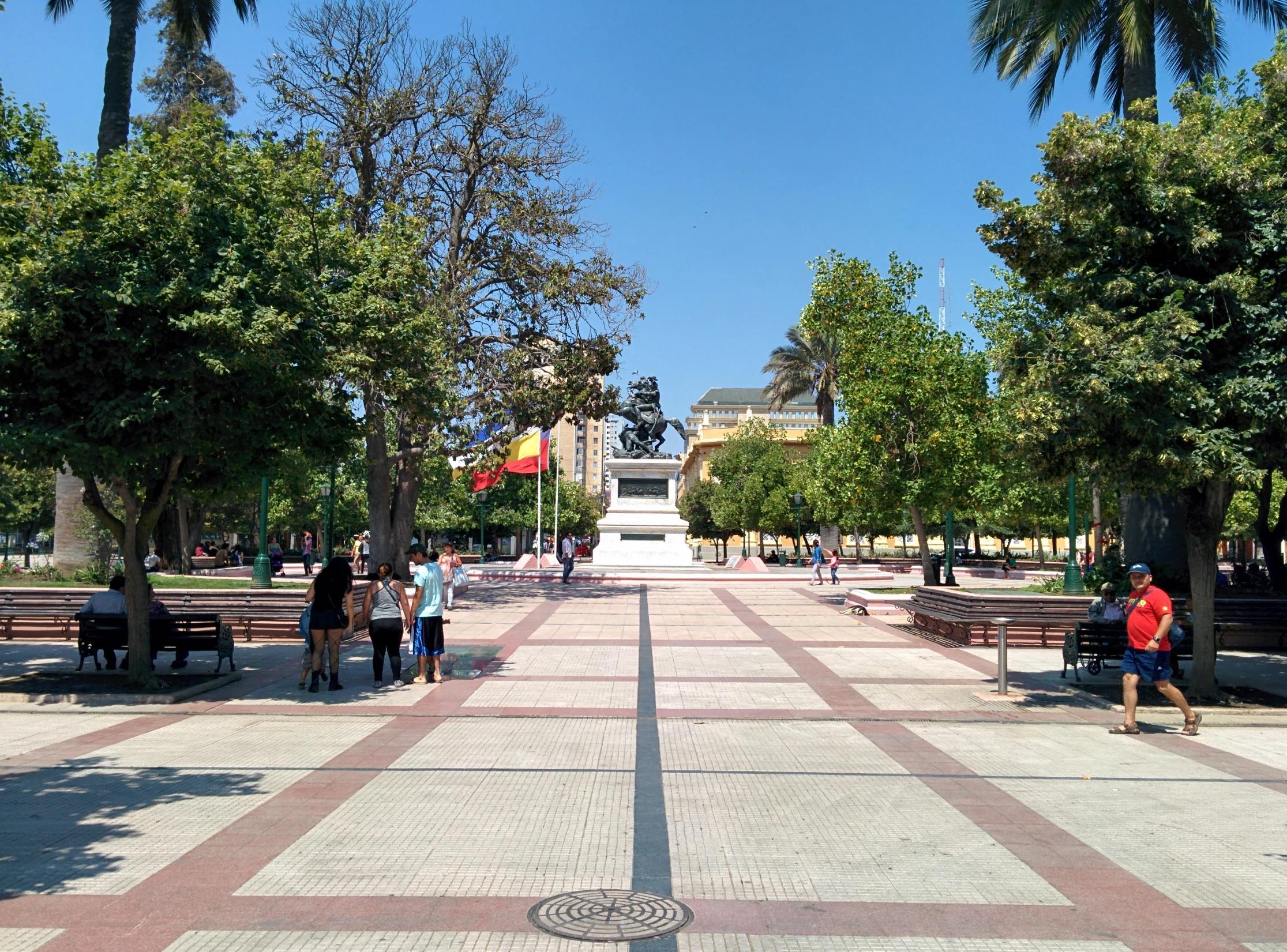 the walkway between two rows of benches leads to several people and a monument