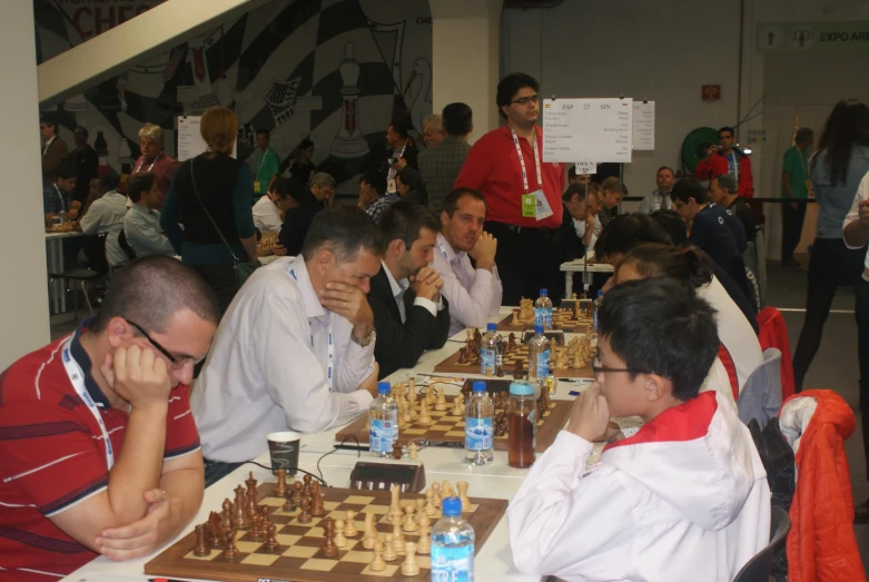 several men and women sit at a long table while playing chess