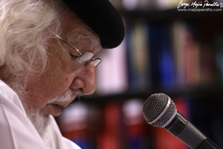 a older man with a long white beard and glasses talks into a microphone