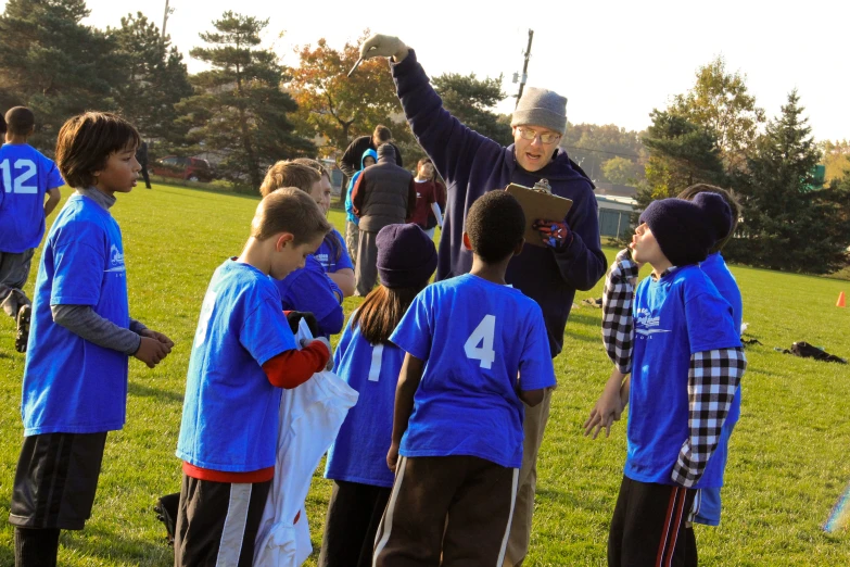 many young children in blue shirts standing around talking to an older man