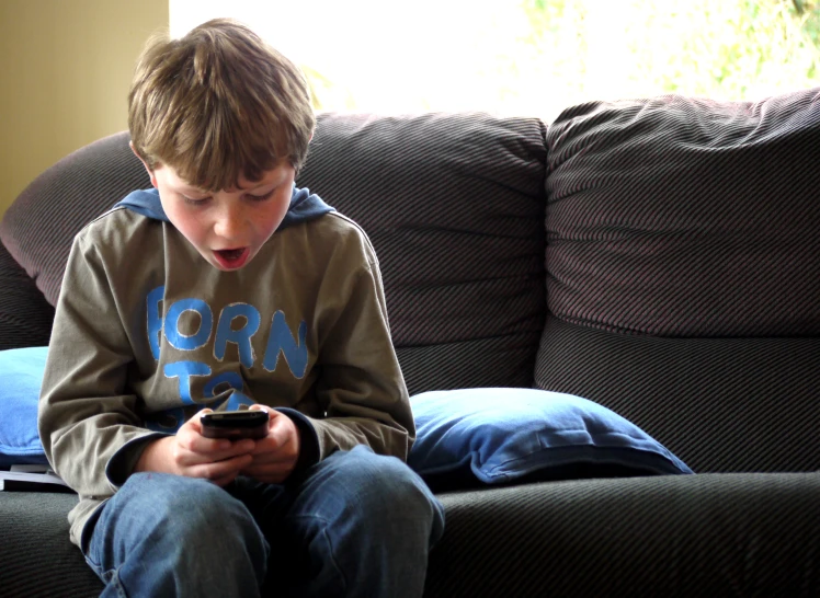 a boy is on his phone while sitting on a couch