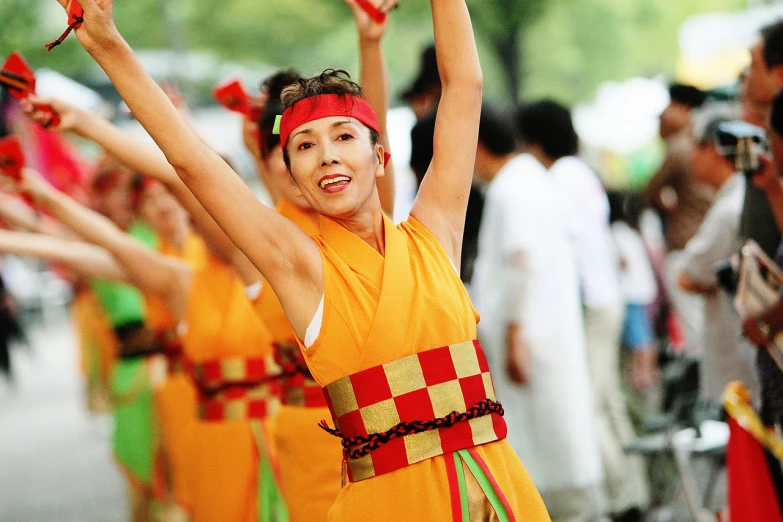 a line of women with red and gold colored dresses dancing on the street