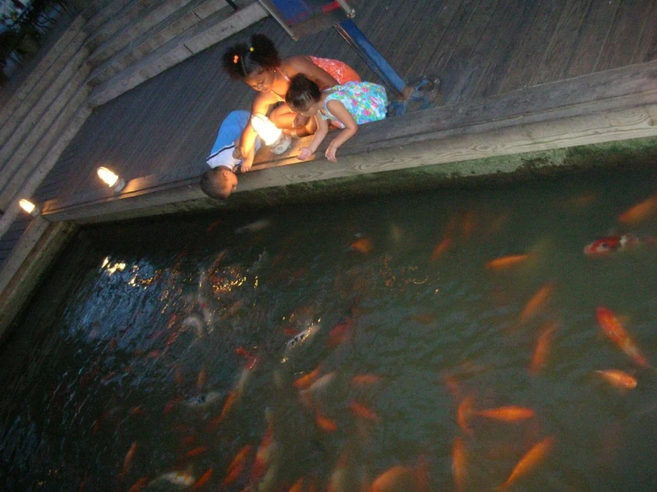 two girls sitting at the edge of a fish pond with goldfish