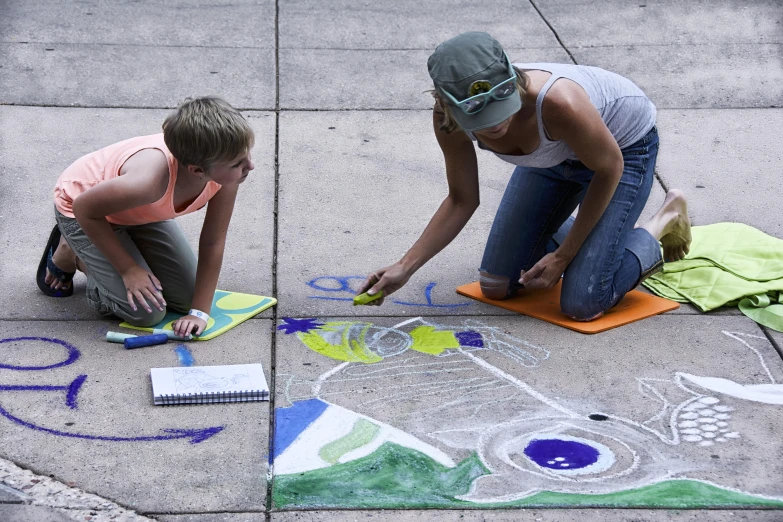 two women are drawing with colorful crayons on the sidewalk