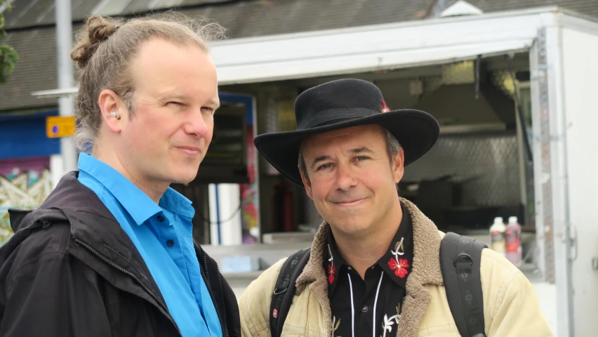 a man wearing a black hat standing next to another man in a blue shirt