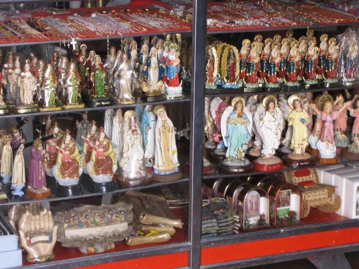 many religious figures and candles sit in a display case