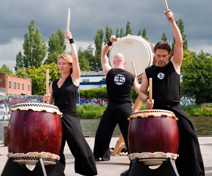 three drummers and a drummer in black with their sticks raised