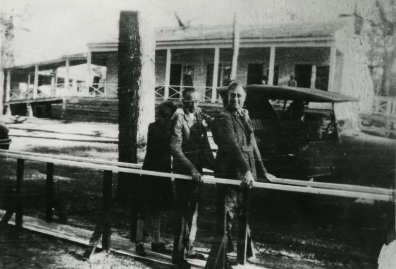 two men are standing on a rail near an old car