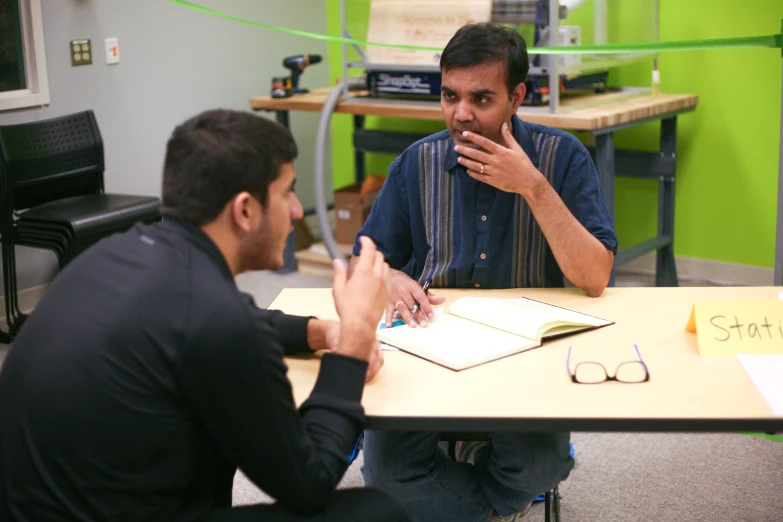 the two men sit at a table looking at soing