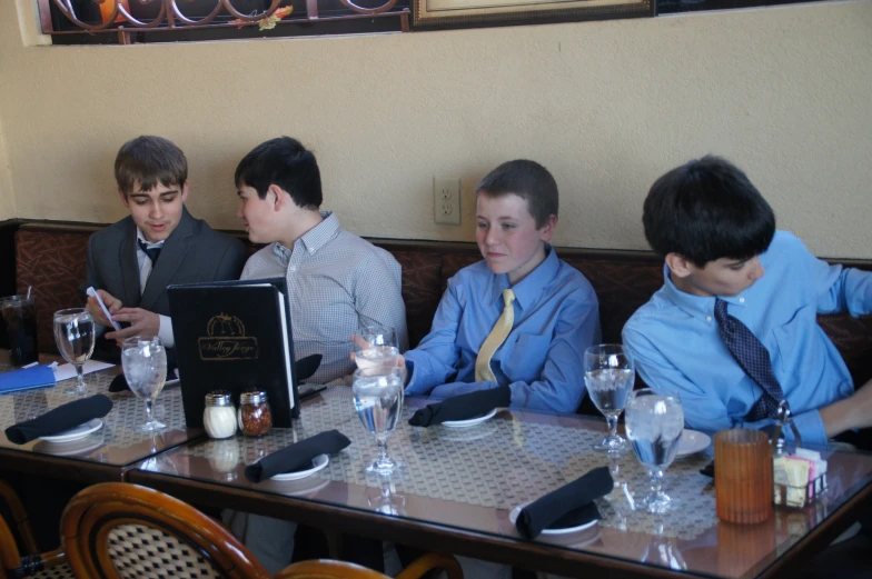 four boys sitting in a restaurant with one man on a computer