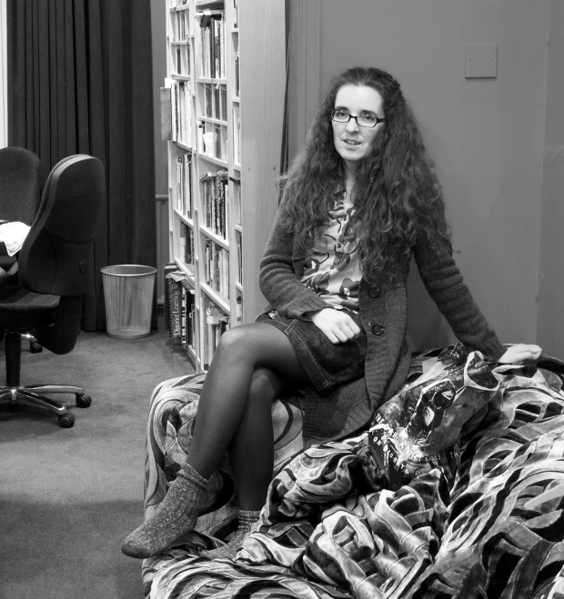 a woman with long hair sits on a chair in front of some books