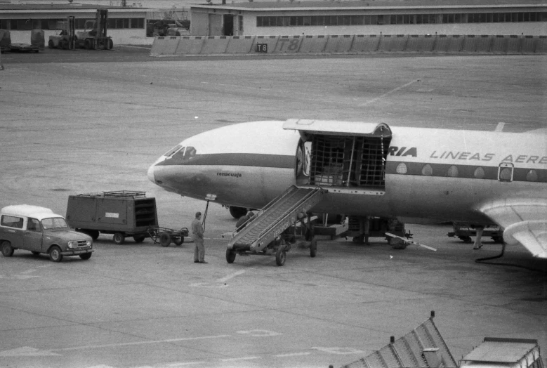 an airplane sits at an airport as a cargo cart walks next to it