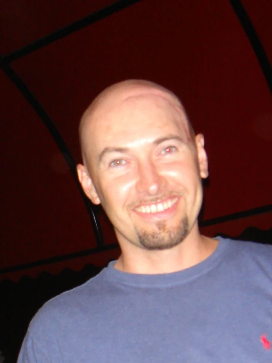 man with a bald head and blue shirt standing under a red umbrella