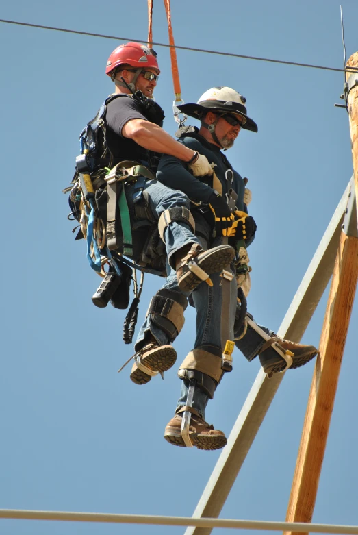 a man on a rope with a helmet on and another on a ladder attached to him