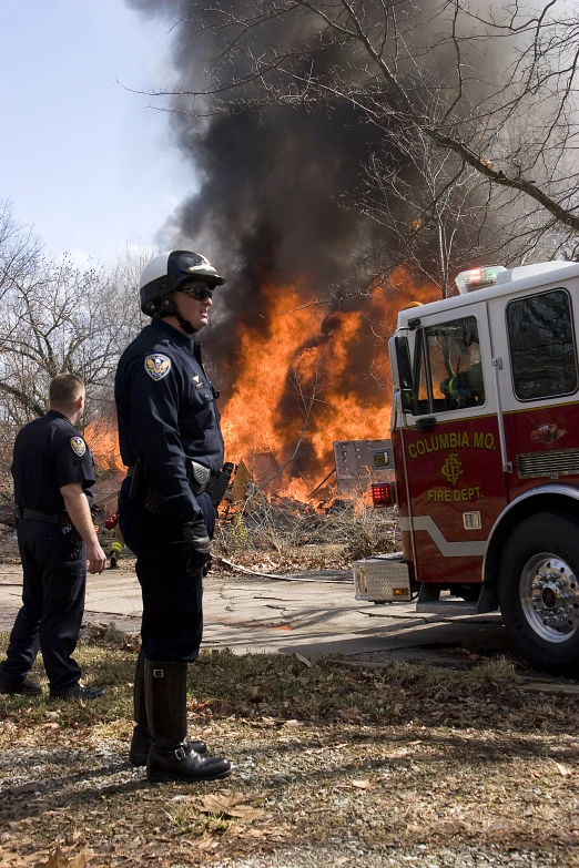 two fire fighters are looking at a blaze in the background