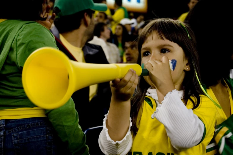 a young woman wearing a michigan fan outfit holds a yellow megaphone up to her mouth