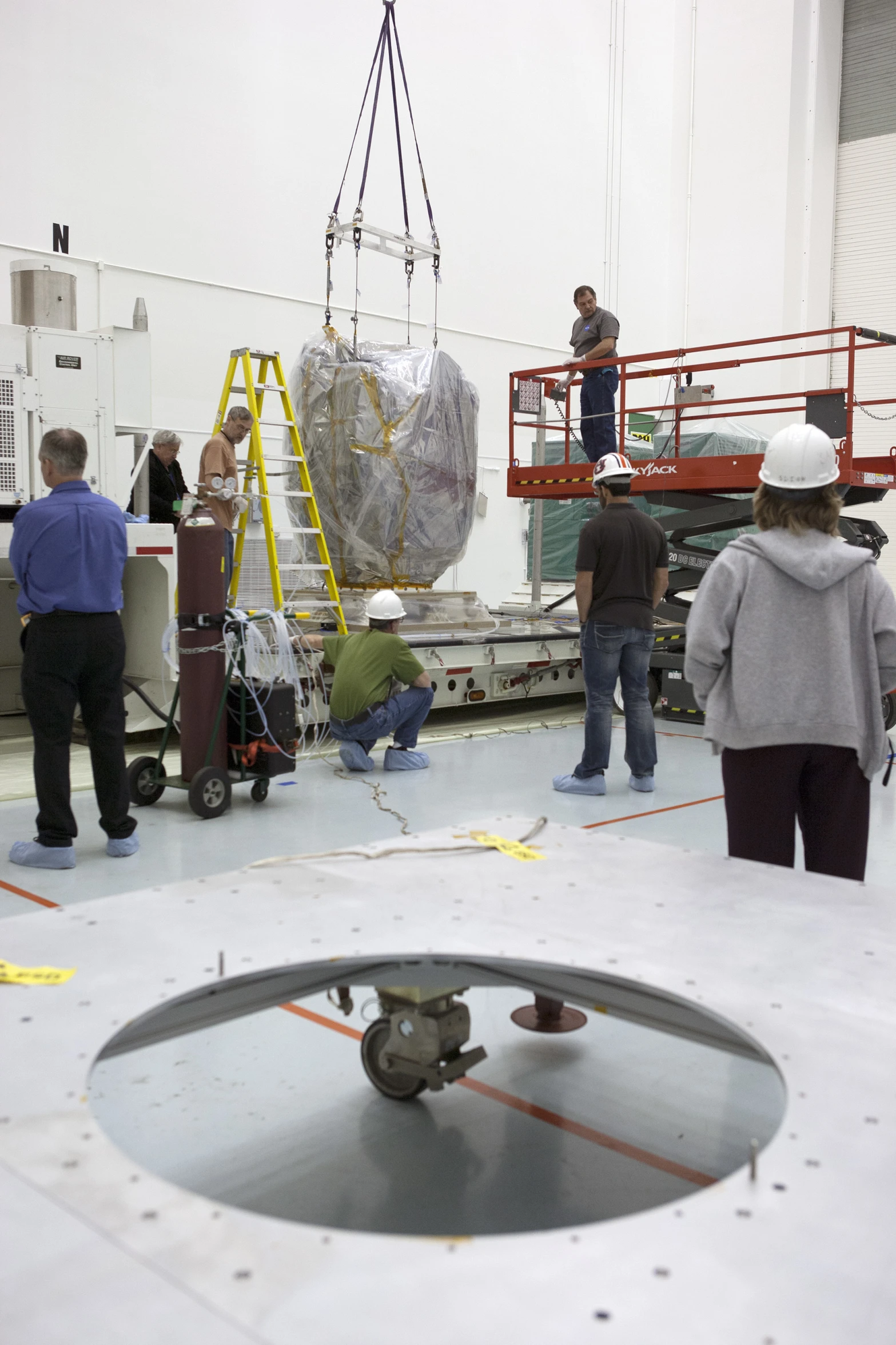 men are working in an industrial facility as one man in grey jacket watches